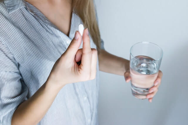 Woman holding glass of water and pill